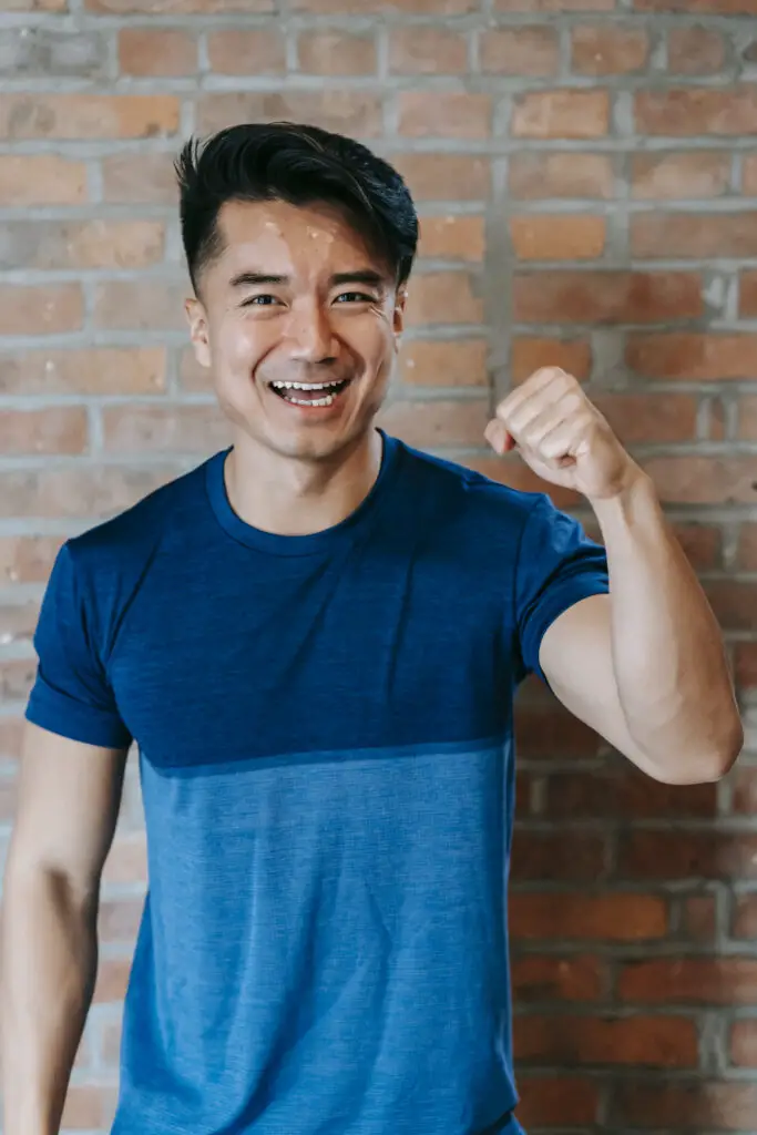 Satisfied young asian sportsman showing biceps and smiling
